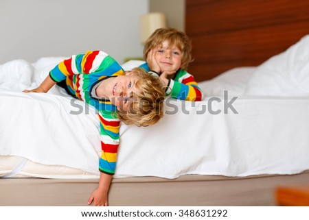 Two adorable little sibling kid boys having fun in bed after sleeping at home, indoor. Brothers smiling at the camera. Family, vacation, childhood concept. Selective focus on one child