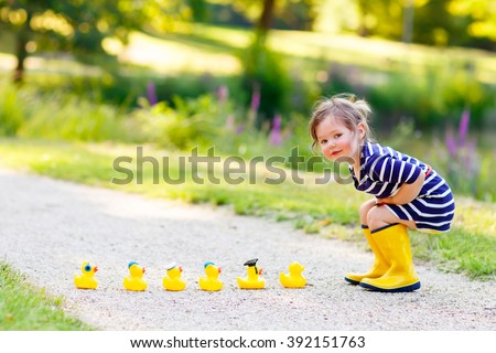 Adorable little kid girl playing in forest playground with yellow rubber ducks. Cute child wearing rain boots. Active leisure with kids.