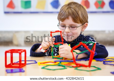 Little child playing with lots of colorful plastic blocks kit in preschool nursery. Happy kid boy having fun with building and creating geometric figures and learning mathematics