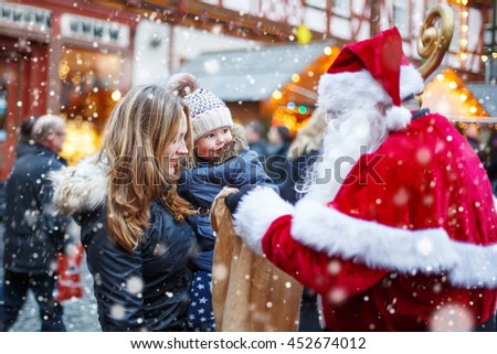 Cute toddler girl with mother on Christmas market. Funny happy kid taking gift from bag of Santa Claus. holidays, christmas, childhood and people concept. Happy family during snowfall on winter day.