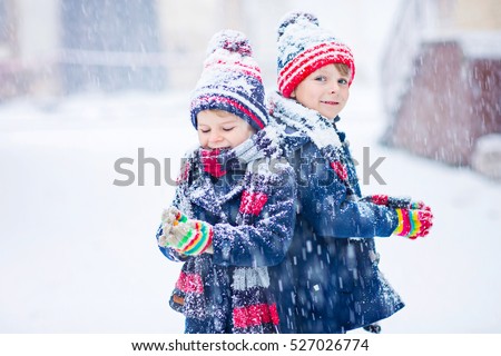 Two little kid boys in colorful clothes playing outdoors during snowfall. Active leisure with children in winter on cold days. Happy siblings and twins having fun with snow