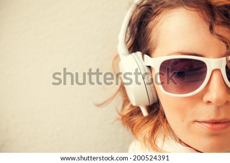 Beautiful young woman in a sunglasses and headphones listening music near the wall