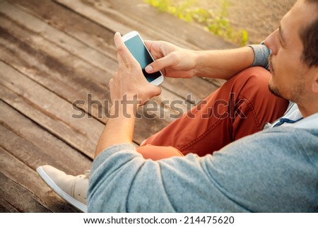Young  hipster man using smart phone sitting on wooden boards