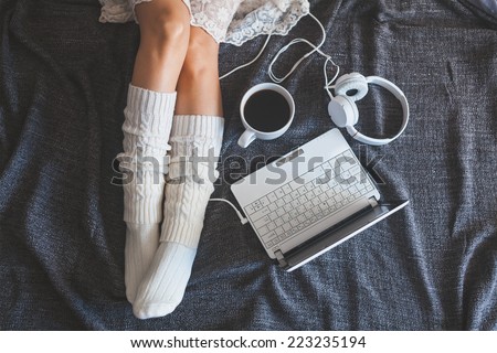 Soft photo of woman on the bed with notebook, headphones and cup of coffee, top view point