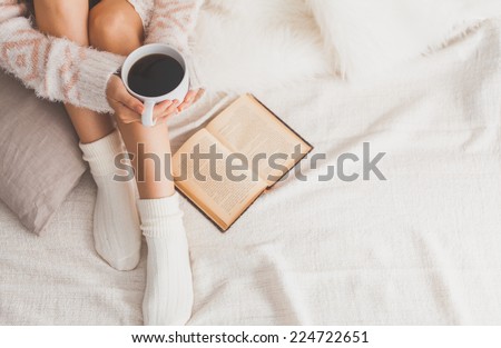 Soft photo of woman on the bed with old book and cup of coffee in hands, top view point. Cozy, comfy, soft