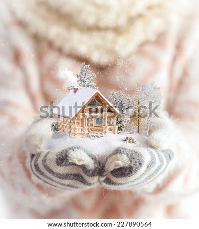 Young woman in mittens holding snow in her hands with a log house. Unusual christmas concept