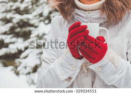 Young woman in red gloves is holding the cup of tea in her hands