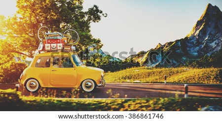 Cute little retro car with suitcases and bicycle on top goes by wonderful countryside road at sunset