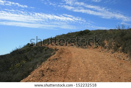 Dirt road leading up a hill side beneath blue sky with clouds, Malibu, CA