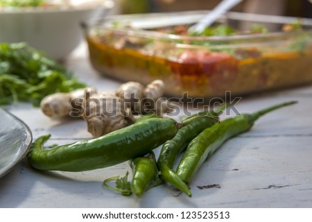 Fresh chili and ginger on white table with typical indian food on background