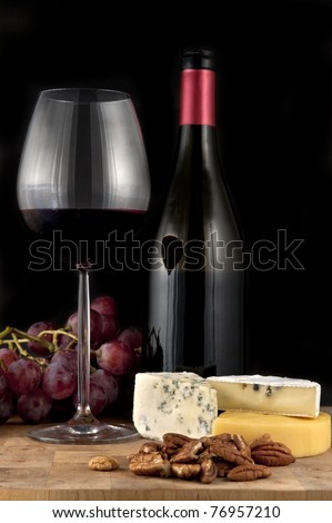 Glass of red wine with bottle and food on black background
