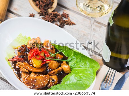 pieces of chicken cooked in black bean sauce on a wooden table in a restaurant with white wine and decorated with an Asian background