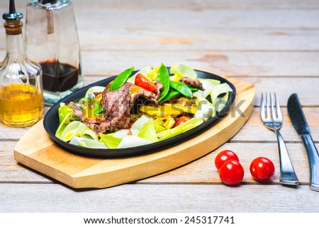 slices of beef with vegetables on a hot pan in a restaurant on a wooden table with an Asian background