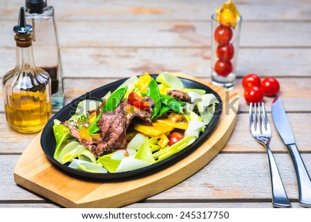 slices of beef with vegetables on a hot pan in a restaurant on a wooden table with an Asian background
