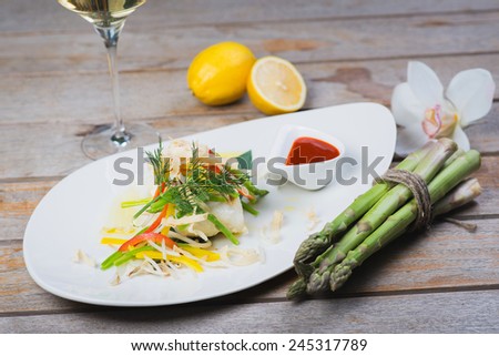 serving of steamed sea bass fillet on a plate in a restaurant, on a wooden table with white wine and decor