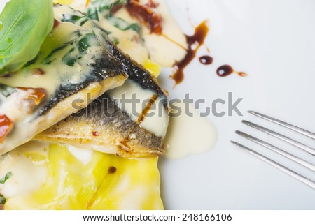 traditional Italian ravioli with sea bass fillet served on a plate on a wooden table with decor