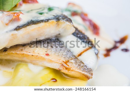 traditional Italian ravioli with sea bass fillet served on a plate on a wooden table with decor