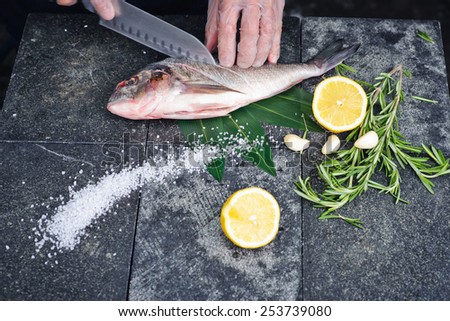Process of cooking Dorado fish with lemon and herbs hands cook cut up the fish on a stone cutting board