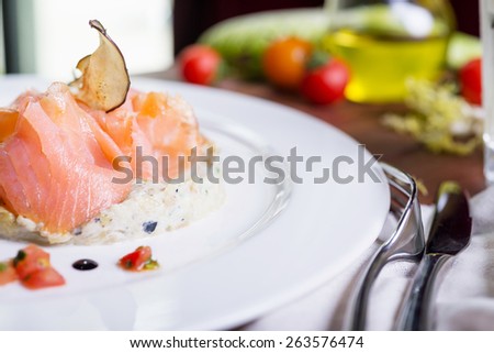 delicious smoked sliced salmon with tartar sauce on a white plate on a wooden table in a restaurant with decor