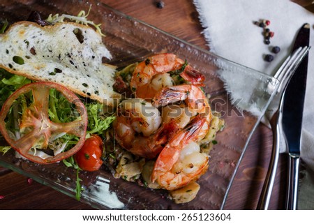 Healthy and fresh salad with shrimps and vegetables serving on the plate on a wooden table in a restaurant with decor