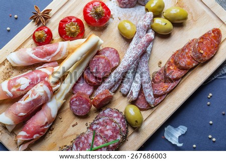 mix of traditional spanish ham salami parma ham on grissini bread sticks, marinated vegetables and olives on wooden plate with rustic decor
