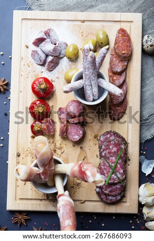 top view of mix of traditional spanish ham salami parma ham on grissini bread sticks, marinated vegetables and olives on wooden plate with rustic decor