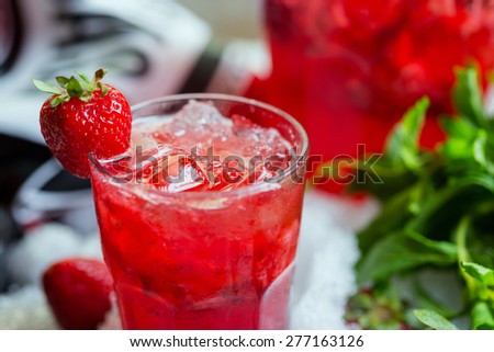 glass of cold fresh summer bright strawberry lemonade on a table with creative composition with ice, strawberries and fresh mint, soft focus
