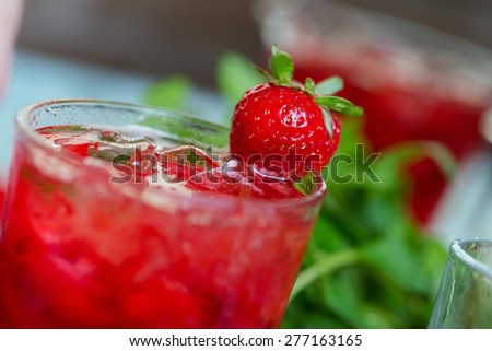 close up glass of cold fresh summer bright strawberry lemonade on a table with creative composition with ice, strawberries and fresh mint, soft focus