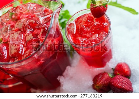 a decanter of bright summer cool refreshing strawberry lemonade on a table with a creative composition with ice, strawberries and fresh mint, soft focus
