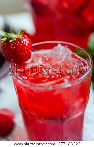 glass of cold fresh summer bright strawberry lemonade on a table with creative  composition with ice, strawberries and fresh mint, soft focus