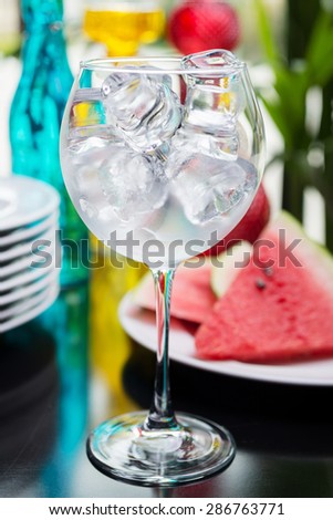 Empty glass filled with ice cubes on a table in the restaurant with the decor of brightly colored dishes and pieces of watermelon. Soft focus