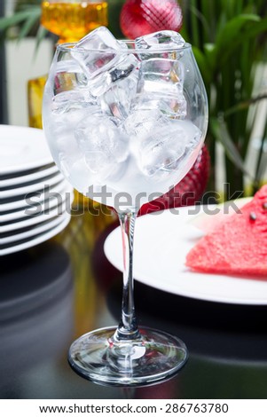 Empty glass filled with ice cubes on a table in the restaurant with the decor of brightly colored dishes and pieces of watermelon. Soft focus