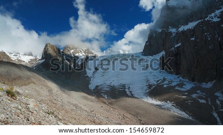 Aksay Glacier in Kyrgyz Mountains with rocks, snow, Ice, and clouds on dark blue sky