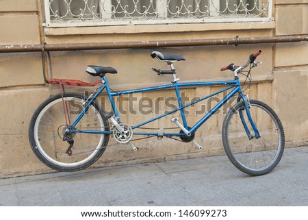A blue tandem bike is parked near a wall