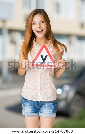 Young teenage learner driver holding U-plate (russian analogue L-plate) and car keys, proud of passing her driving test at school.