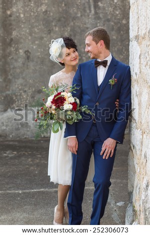 young couple just married people standing near a wall smiling and looking at each other