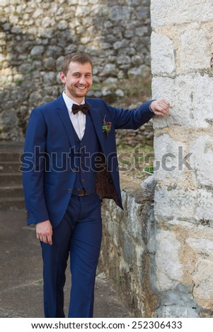 portrait of a handsome groom in a blue suit smiling leaning on the wall
