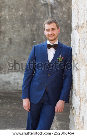 portrait of a handsome groom in a blue suit smiling leaning on the wall