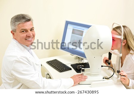 Optometry concept -  young woman having her eyes examined by an eye handsome elderly doctor. Topography of the cornea
