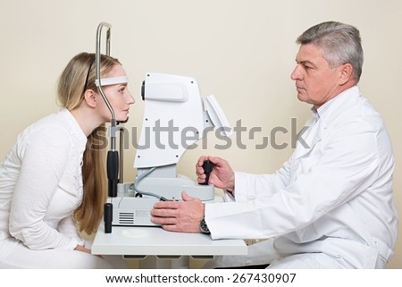Optometry concept -  young woman having her eyes examined by an eye handsome elderly doctor. Topography of the cornea