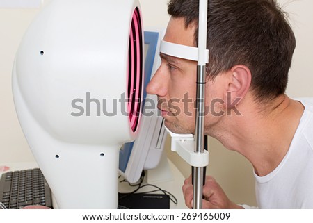 Optometry concept - man having his eyes examined by an eye  elderly doctor. Topography of the cornea.