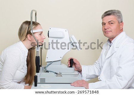 Optometry concept -  young woman having her eyes examined by an eye  elderly doctor.