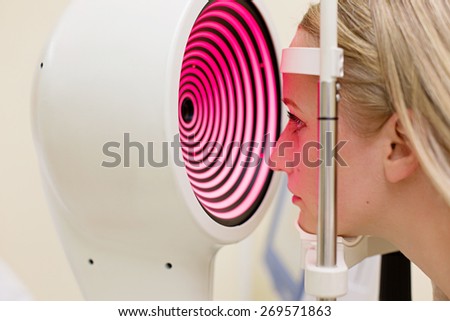 Optometry concept -  young woman having her eyes examined by an eye handsome elderly doctor. Topography of the cornea.