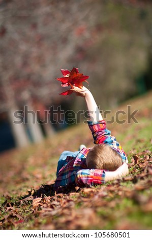 The boy is relaxed on the ground holding an armful of autumn leaves, focus on the leaves