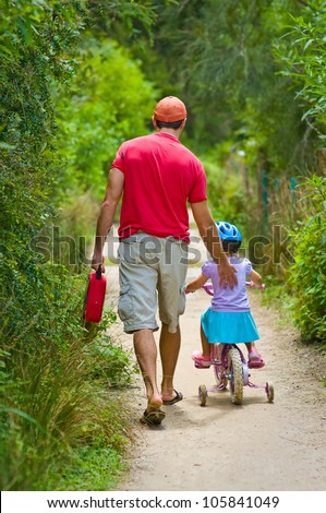 Back view of a father pushing his daughter on a bicycle on a summer day