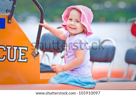 Outdoor portrait of a cute toddler girl sitting in a surf rescue boat