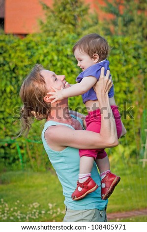 Happy young mother holding up her little daughter on a sunny summer day