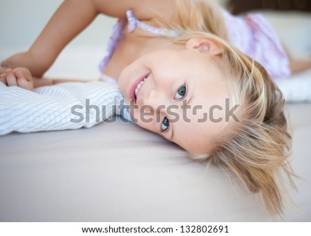 Morning portrait of a happy toddler girl relaxing in her bed with head upside down