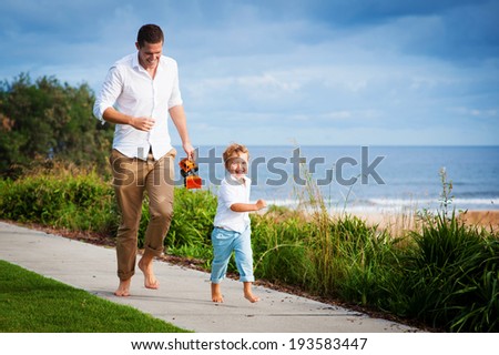 Young dad and son having fun running at the beach footpath in summer