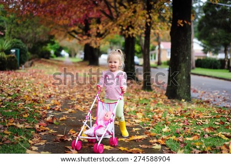 Happy cute child, adorable toddler or baby girl going for a walk with a doll pram and a doll in it in a beautiful park with autumn trees and leaves